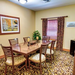 A neatly arranged conference room featuring a wooden meeting table with six chairs and decorative elements like paintings and curtains.