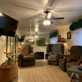 A cozy living room featuring multiple recliner chairs, a ceiling fan, and a fireplace.