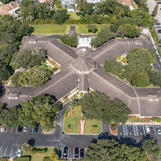 Aerial view of a cross-shaped building surrounded by trees and parking lots.