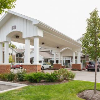 A covered entrance with cars parked in front, surrounded by landscaping and trees.