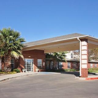 A modern building entrance with a covered walkway and palm trees under a clear blue sky.