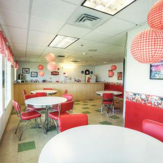 A retro-style diner interior with red and white decor, featuring round tables and chairs.