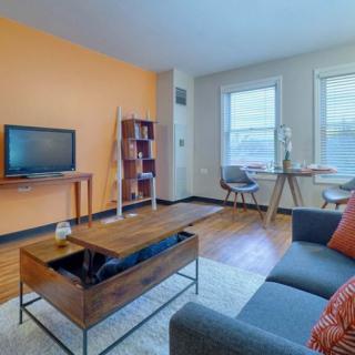 A cozy living room with an orange accent wall, featuring a TV, bookshelf, and work desk.