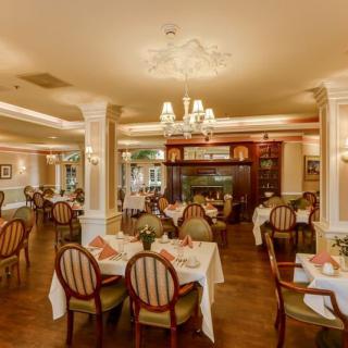 An elegant dining room featuring beautifully set tables, classic chairs, and ornate chandeliers.