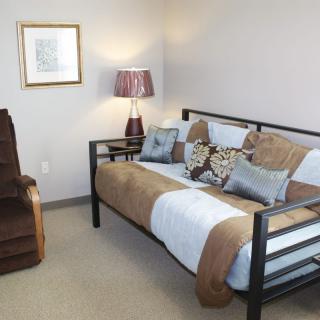 A cozy bedroom featuring a daybed with plush pillows, an armchair, and a decorative lamp.