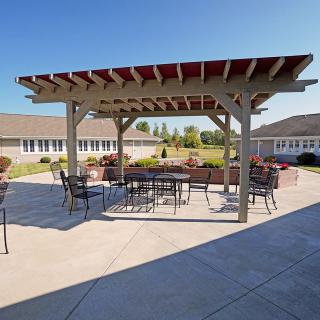 A sunny courtyard featuring a pergola with outdoor seating and tables.