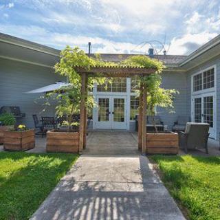 A beautiful patio area with a pergola, surrounded by greenery and outdoor seating on a sunny day.