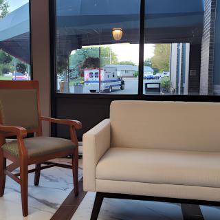 A modern lobby area featuring a beige sofa and a wooden chair near large windows.