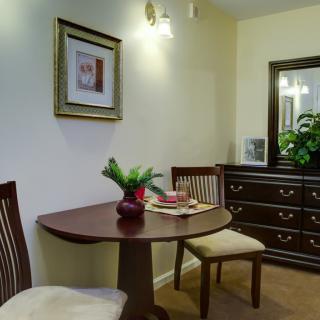 A cozy dining area with a small round table and two chairs, complemented by decorative elements such as framed art, a mirror, and plants.