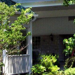 A cozy residential house with a porch surrounded by lush greenery.