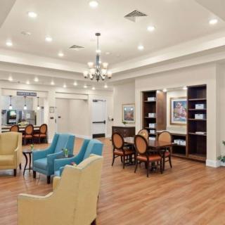 A spacious and well-lit lounge with comfortable seating, chandeliers, and a bookshelf.