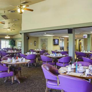 A brightly lit restaurant dining area featuring purple chairs and set tables.
