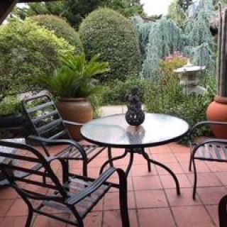 A cozy patio with a table and chairs, surrounded by lush garden greenery.