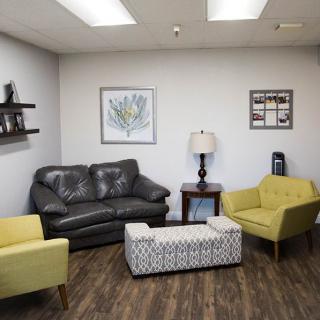 A cozy living room with a black sofa, two yellow chairs, and wall art.