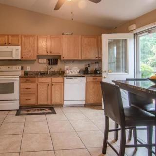 A spacious kitchen with wooden cabinets, featuring modern appliances and a dining area with an open door leading outside.