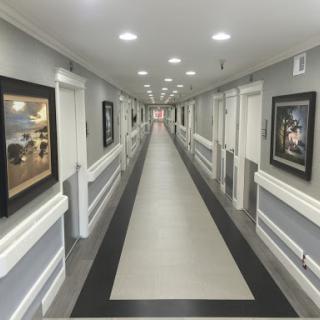 A modern hallway featuring gray walls, illuminated ceiling lights, and framed artwork along the sides.