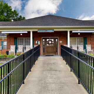 A brick building entrance with a ramp leading up to the front door, flanked by large windows.