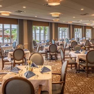 An elegant dining room with neatly arranged tables and chairs, featuring large windows.