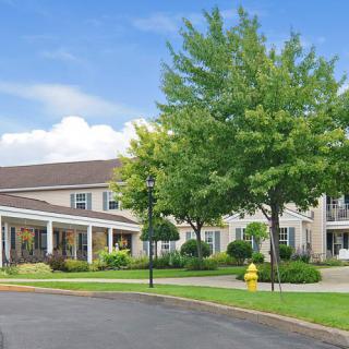A well-maintained residential building surrounded by trees and a driveway under a clear blue sky.