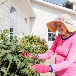 A woman enjoying a sunny day gardening outside her home.