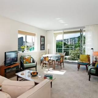 A bright living room with comfortable furniture, a table set near large windows, and access to a balcony.