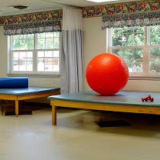A spacious therapy room featuring a bright red exercise ball and two treatment tables.