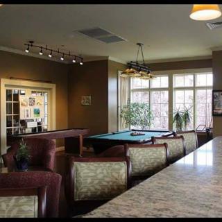 A cozy lounge area featuring a pool table and comfortable seating, illuminated by natural light from large windows.