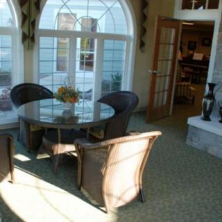 A sunlit dining area featuring a round glass table surrounded by wicker chairs, with large arched windows providing natural light.