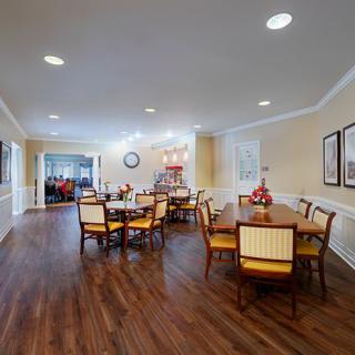 A spacious dining room with wooden flooring and neatly arranged tables and chairs.