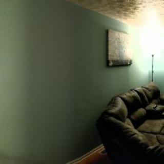A cozy living room with a couch, painting, and floor lamp against a green wall.
