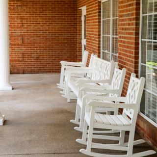 A row of white rocking chairs lined up on a porch against a brick wall, inviting relaxation.