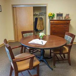 A cozy meeting room featuring a round wooden table with four chairs, a coat rack, and a floral arrangement on the table.