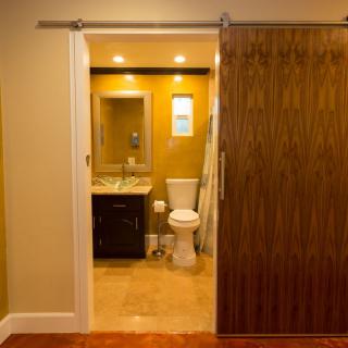 A modern bathroom with a sliding wooden door, featuring a sink, toilet, and warm lighting.
