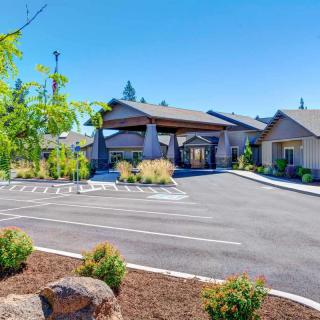 A modern building with a spacious parking area surrounded by landscaped greenery and clear blue skies.