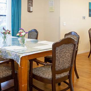 A cozy dining room with a wooden table, upholstered chairs, and decorative flowers.