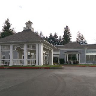 A view of a charming architectural structure featuring white pillars and a quaint roof, set in a landscaped environment.