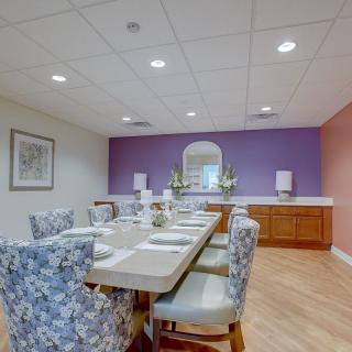 A well-decorated dining room with a long table and upholstered chairs, featuring a purple accent wall.