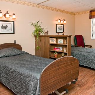 A cozy bedroom with a neatly made bed, a cushioned chair, and wooden furniture against a warmly painted wall.