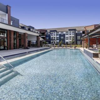 An inviting swimming pool at a modern apartment complex under a clear blue sky.