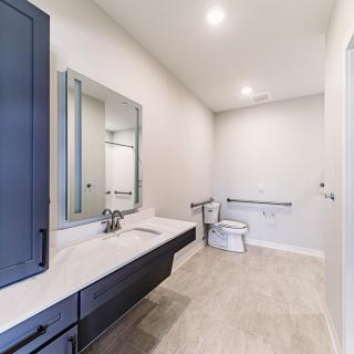 A modern, minimalist bathroom featuring a large vanity with a mirror, toilet, and ample lighting.