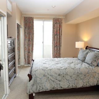 A cozy bedroom featuring a neatly made bed, a lamp on the nightstand, and tall curtains framing a window.