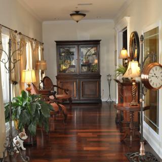A well-decorated hallway with hardwood flooring, featuring elegant furniture, lamps, and plants.