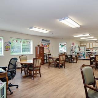 A spacious community room with tables and chairs, featuring a kitchen area and large windows providing ample natural light.