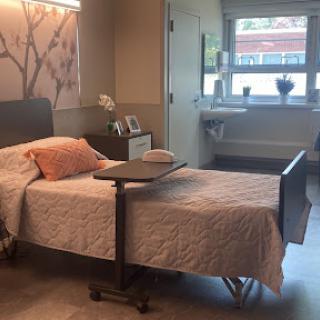 A well-lit hospital patient room featuring a bed, a bedside table, and a view of the outside.