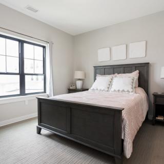 A modern bedroom with a large bed, gray walls, and natural light from a window.