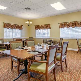 A well-lit dining area with neatly arranged tables and chairs, featuring windows with decorative curtains.