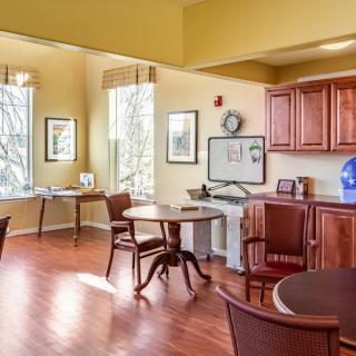 A cozy dining area with wooden tables and chairs, featuring warm wood flooring and natural light from large windows.