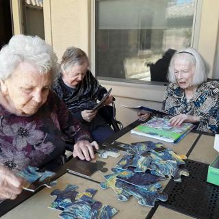 A group of elderly women working on a puzzle together outdoors.