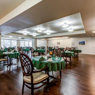 A spacious dining room with green tablecloths and wooden chairs arranged neatly on a wooden floor.