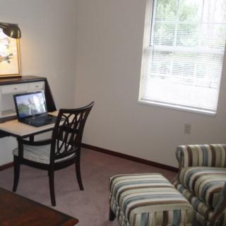 A cozy home office with a desk, chair, laptop, window, armchair, and ottoman.